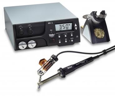 The image shows a soldering device with a control unit. It has a digital display, two round knobs, and a soldering iron with a cable. Next to the soldering iron, there is a holder.