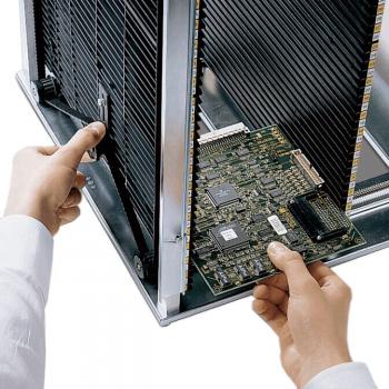 Eine Person hält eine Computerplatine in der Hand und steckt sie gerade in ein metallisches Gehäuse. Im Hintergrund sind Kühlerstreben sichtbar. Der Fokus liegt auf der Platine.