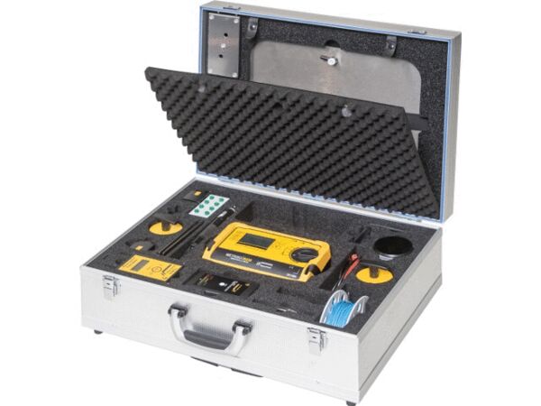 The image displays an open, silver suitcase. Inside, there is a yellow device, numerous buttons, cables, and compartments, all neatly organized in a foam-padded interior.