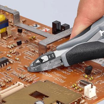 In the picture, you can see a hand holding a pair of pliers. It is being used to work on an electronic circuit board that has many small components and traces on a brown surface.