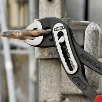 The image shows a Knipex pliers attached to a metal fence. The pliers are gripping a rusty key that is slightly protruding from the fence.