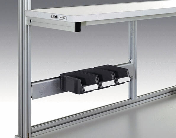 The image displays a metal structure with a horizontal rail profile. Below it, three black compartments are attached, which are likely used for storage or holding items.
