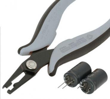 Das Bild zeigt eine spezielle Zange mit flachen, spitzen Backen, ideal für Elektronikarbeiten. Neben der Zange liegen zwei schwarze Kondensatoren mit zwei Metallstiften.