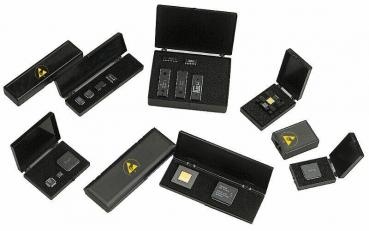 The image shows a black, rectangular box with a circular, yellow logo depiction on the top. On the front, there is a small lever or button.