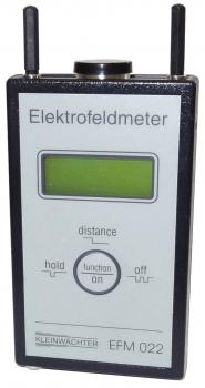 The image displays a digital electrofield meter. It features a rectangular shape, a gray front with a large display in the center, and two antennas on top. Buttons are arranged below it.