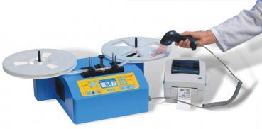 The image shows a blue device with two round discs on top and a printer next to it. A hand is holding a barcode scanner. The device has a display and buttons for operation.