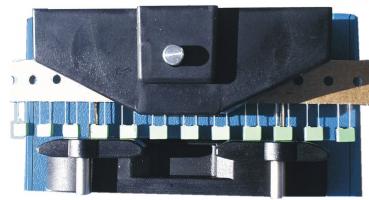 The image shows a device with a black top part and a blue base. Below, two round rollers are visible. On the side, there are several green and white switches or buttons.