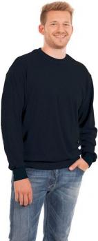 Ein lächelnder junger Mann trägt einen schwarzen Pullover und hellblaue Jeans. Er steht entspannt mit einer Hand in der Hosentasche und hat die andere leicht an der Hüfte.