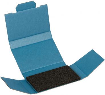 Das Bild zeigt eine blaue Verpackung, die geöffnet ist. In der Mitte liegt ein schwarzes, rechteckiges Stück, möglicherweise Schmirgelpapier oder ähnliches Material. Die Verpackung hat gefaltete Flächen.