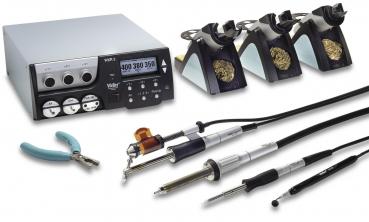 The image displays a toolkit with a control unit, multiple soldering tips, pliers, and various soldering tools. Everything is arranged on a work surface.