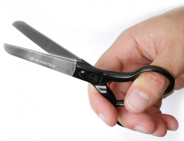 The image shows a hand holding a black pair of scissors. The scissors have two shiny blades and an ergonomic handle. The name "BERNSTEIN" is embossed on the blade.