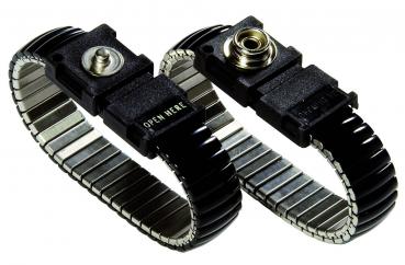 Das Bild zeigt ein schwarzes, metallisches Armband mit einer flexiblen, federnden Struktur. In der Mitte befindet sich ein rechteckiger Verschluss mit der Aufschrift 