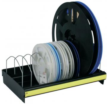 The image shows a black holder with several large, round film reels. One reel is on it, the others are arranged in a row. The holder has a yellow lower edge.