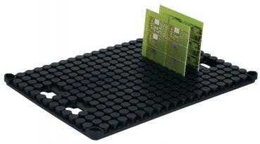 The image displays a black, rubberized mat with many small, round bumps. On it lies a green circuit board, which stands out due to its rectangular shape and several patterns.