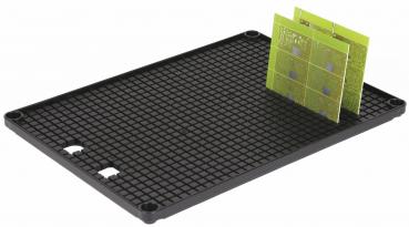 The image shows a rectangular, black plate with a grid pattern. On it is a green, thin piece with square fields, which is slightly tilted.
