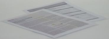 Das Bild zeigt zwei übereinanderliegende Blätter Papier. Das obere Blatt enthält Tabellen oder strukturierte Daten, während das untere Blatt Text in schriftlicher Form hat.
