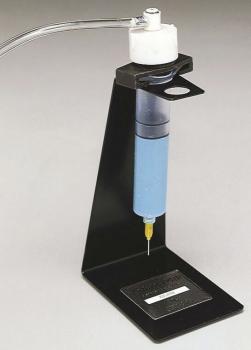 The image shows a device with a cylindrical blue container mounted on a black stand. There is a black cap on top connected to a hose.