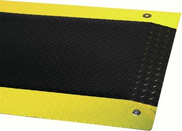 The image shows a non-slip mat with a black, textured surface, surrounded by a yellow edge. The corners are reinforced and there are screws for mounting.