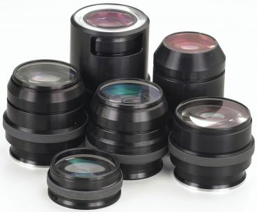 The image displays multiple black camera lenses in various sizes and shapes. Some lenses feature a shiny, transparent surface, while others are matte. They are artfully arranged.