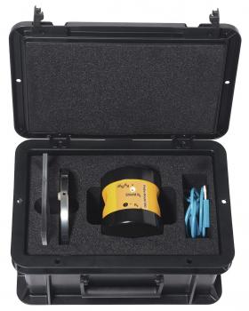 The image shows a black suitcase, open, with a special foam insert. Inside, there is a round, black object with yellow lettering, a metallic bracket, and two blue cables.