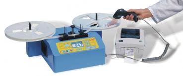 The image shows a blue device with two round plates on top, a display and buttons in the middle. To the right, there is a printer. A hand is holding a scanner, which is pointing at a label.