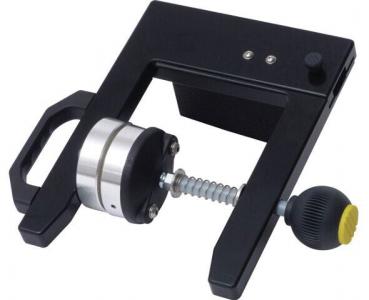 The image displays a black device with a textured grip and a round push element. It features an adjustment screw and a spring mechanism that ensures precision.