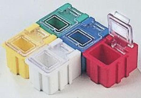 Das Bild zeigt fünf kleine, quadratische Kunststoffboxen in verschiedenen Farben: Gelb, Grün, Blau, Weiß und Rot. Einige haben transparente Deckel. Sie sind stapelbar und haben abgerundete Kanten.
