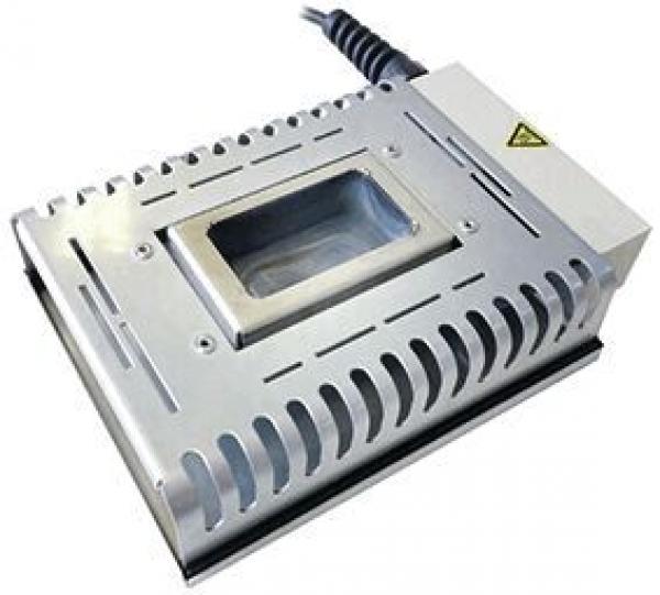 The image shows a silver, rectangular device with a central, rectangular opening. It has a smooth surface, ventilation holes, and a cable on the left side.