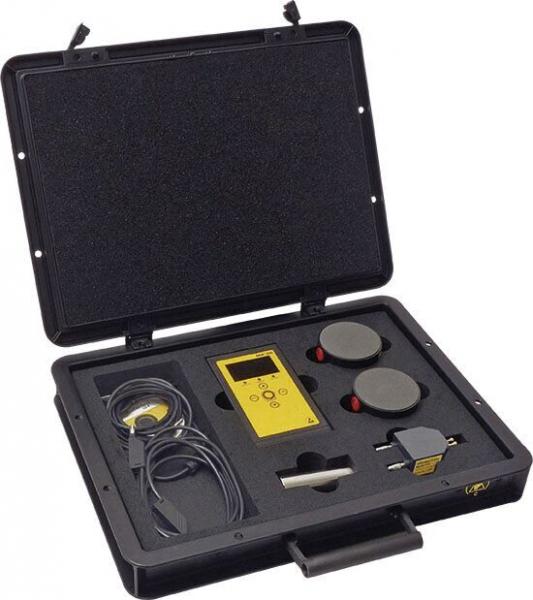 The image shows an open, black suitcase. Inside, there is a yellow device with a display, two round buttons, a cable, and another device. Everything is neatly arranged.