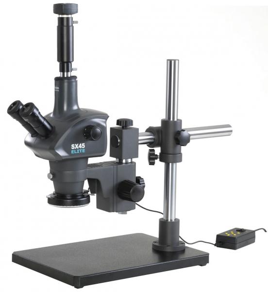 The image shows a microscope with a stable base. It has two eyepieces, an elongated objective, and a rotatable stage. A cable runs from the base. It is in dark gray.