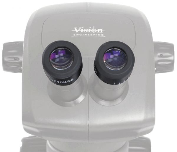 The image shows a binocular microscope with two large, round eyepieces. The surface is light gray with the "Vision Engineering" logo at the top. It has a compact shape.