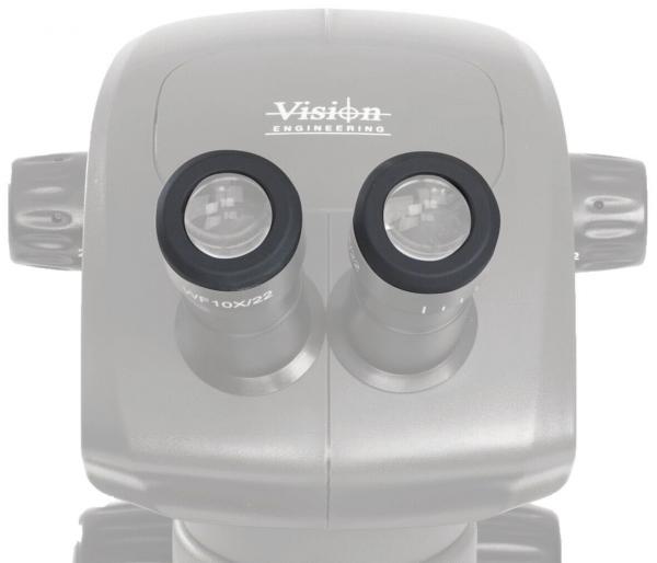 The image shows a microscope with two round eyepieces. The surface is smooth and oval. At the top, it reads "Vision Engineering". It is a technical device for magnifying objects.