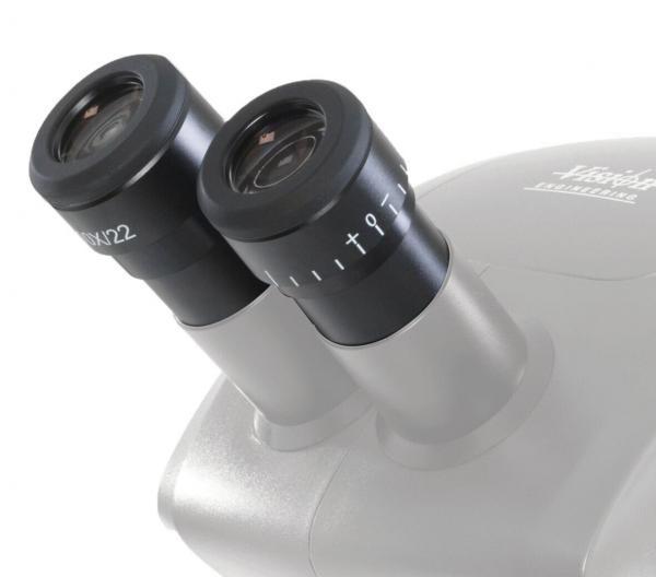 The image shows a microscope attachment with two round eyepieces. The eyepieces are black with numbers and a possible magnification factor. The body is silver-colored.