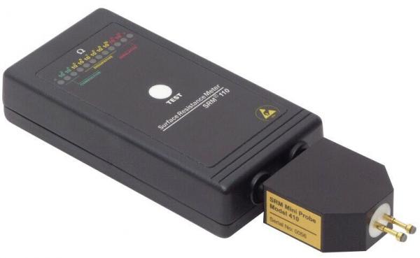 The image displays a black rectangular electric testing device with a plug. At the top, colorful LEDs and a pressed button are visible. It is used for checking electrical connections.