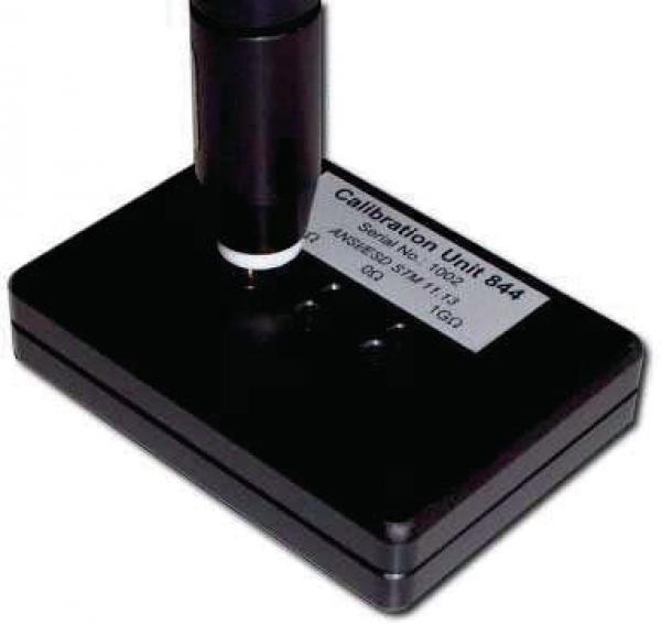 Das Bild zeigt ein schwarzes Kalibriergerät mit einer vertikalen, zylindrischen Säule. Auf der Oberfläche befindet sich ein Etikett mit der Aufschrift "Calibration Unit 844".