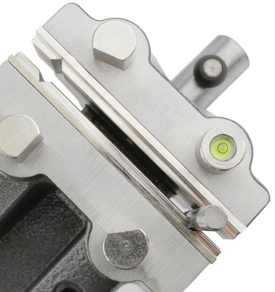 The image shows a metallic device with smooth, edged surfaces. There are screws, a level indicator, and a small cylinder. The surface is partly matte, partly glossy.