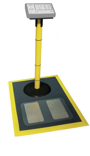 The image displays a digital scale with a vertical, yellow stand. A display is mounted at the top. The weighing area is rectangular, featuring two flat, gray surfaces.