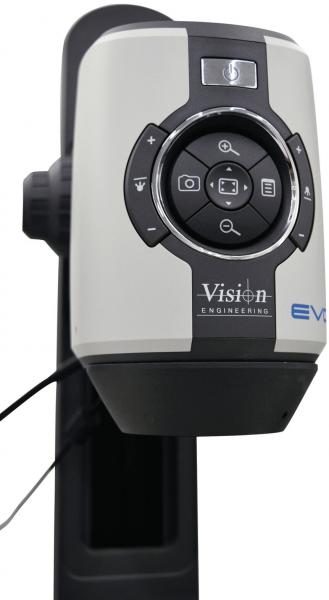 The image shows a device for optical magnification. It has a round, central button with several control knobs around it and is mounted on a stable, black stand.
