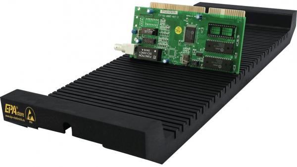 The image displays an elongated, black cooler with grooves and a green computer component resting on top. The card features black and silver components and shiny connections.