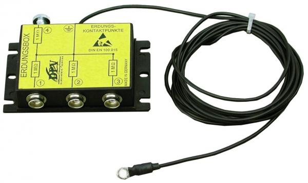 The image displays a black grounding box with three terminals. On the top side, there is a yellow label with symbols and text. Adjacent to the box, there is a black cable with a round connector.
