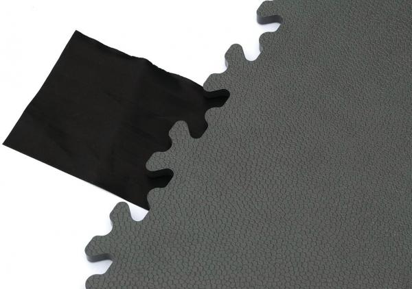 The image displays a matte, green surface with a jagged edge, next to which lies a piece of black fabric. The mat has a textured surface that appears to be slip-resistant.
