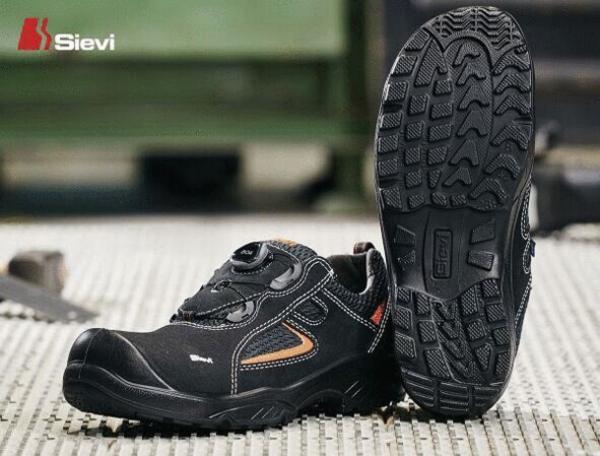The image shows a pair of black safety shoes with a non-slip sole. They are lightweight and feature orange design elements. The sole has a deep tread for better grip.