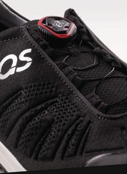 The image shows a black sports shoe with a tight, breathable material and lacing adjusted by a red-black push button. A logo is visible.