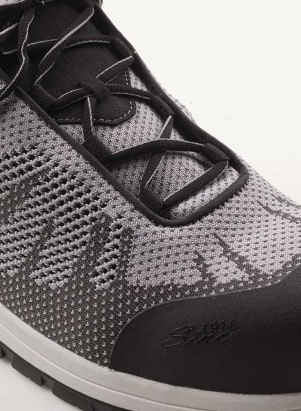 The image shows a sporty shoe in gray and black with breathable mesh material. The laces are black, and the sole is slightly raised.