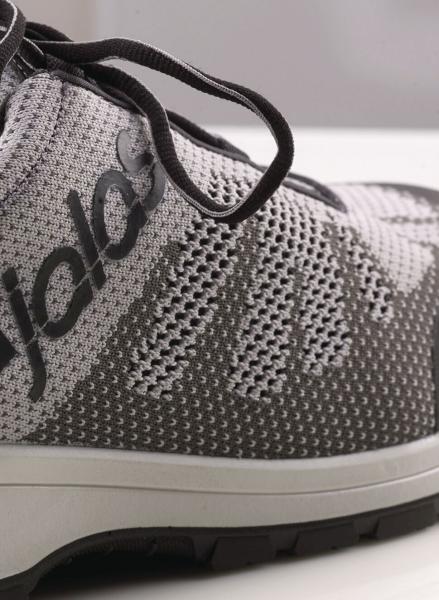 The image shows a gray sports or running shoe. It features a breathable, knitted upper with a subtle pattern and gray laces. The shoe has a light-colored sole.
