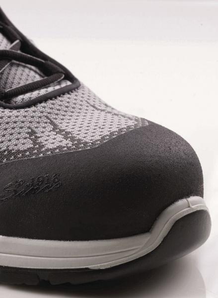 The image shows the tip of a gray shoe with a solid, black cap. The upper material is made of a loose, breathable fabric. Laces run across the shoe.