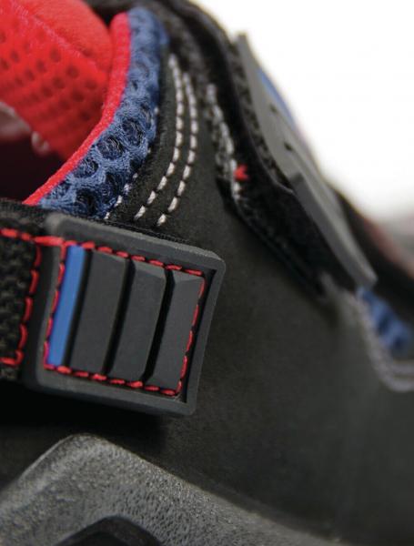 The image shows a close-up of a shoe. The shoe is black with blue and red accents. A buckle and stitching are visible, the fabric appears sturdy and sporty.