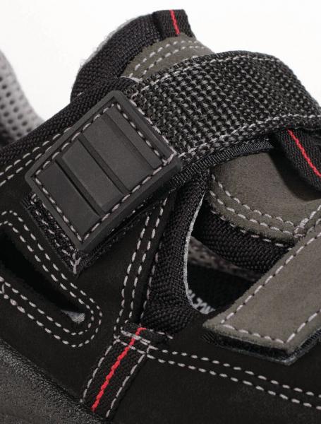 The image shows a black shoe with gray and red accents. It has an adjustable mesh strap and a textured sole. The shoe appears sturdy and sporty.