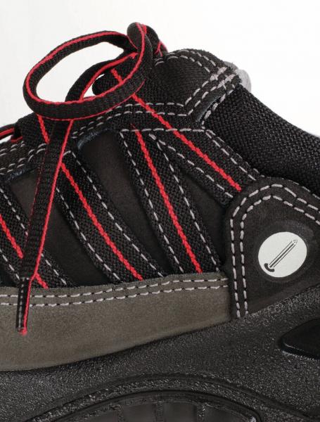 The image shows a black shoe with red and gray accents. The surface is made of fabric with a mesh design, and the laces are loosely tied. The shoe has a sturdy sole.