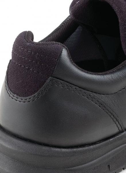 The image shows the back of a black sneaker. The shoe is made of a smooth leather surface and has a padded, dark blue collar.